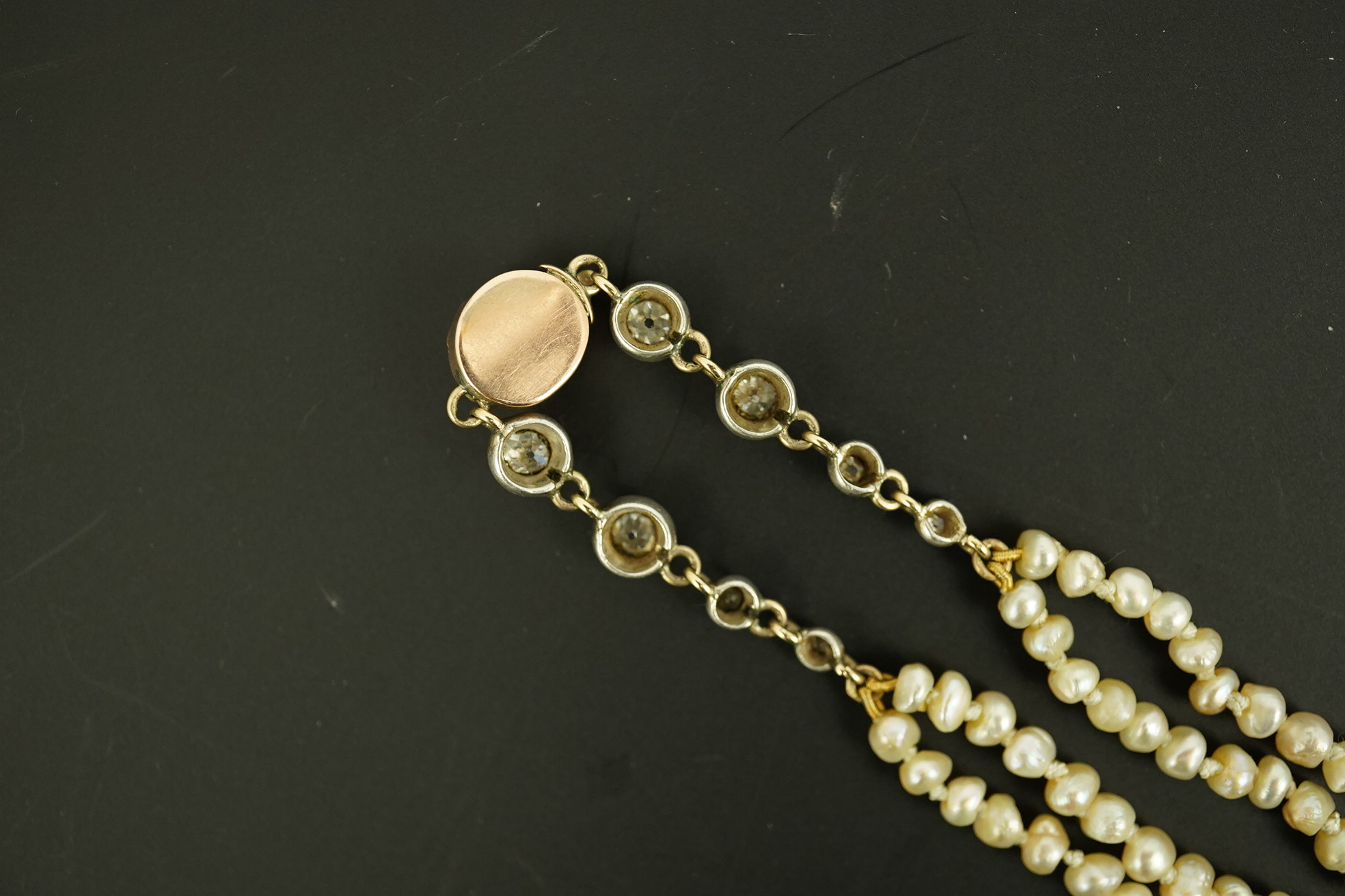 An antique twin strand baroque pearl necklace, with pearl set gold clasp bordered with single chain set with four graduated old mine cut diamonds